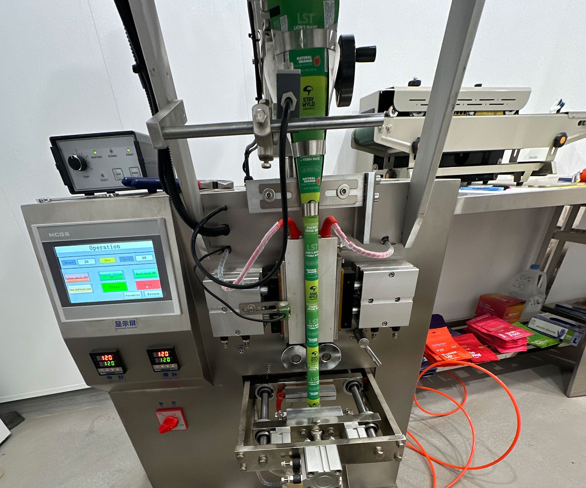 An industrial automatic liquid-filled pouch packaging machine with a digital control panel, metal components, and green plastic components, shown in a workshop setting.